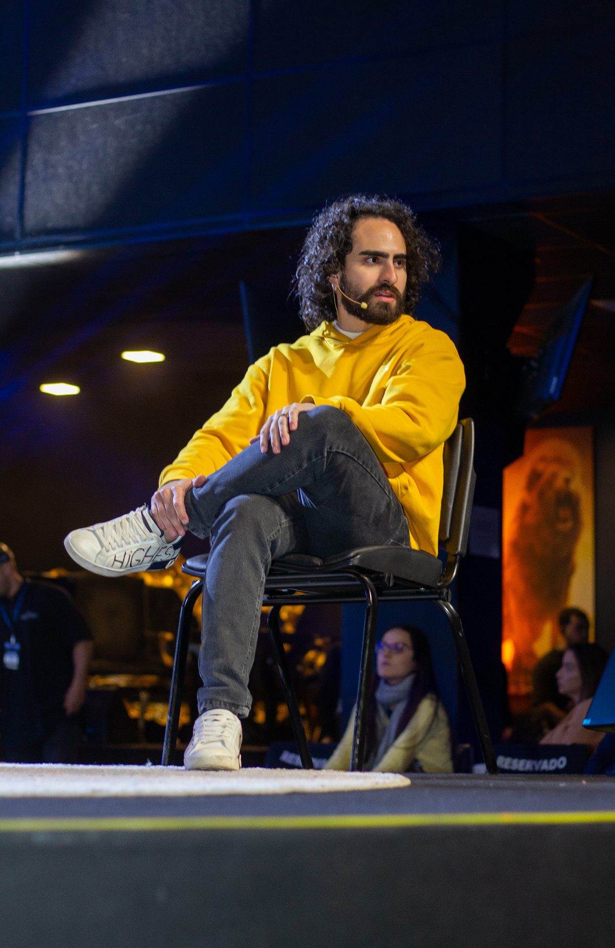 Euriler sentado no palco, falando com a plateia num evento presencial